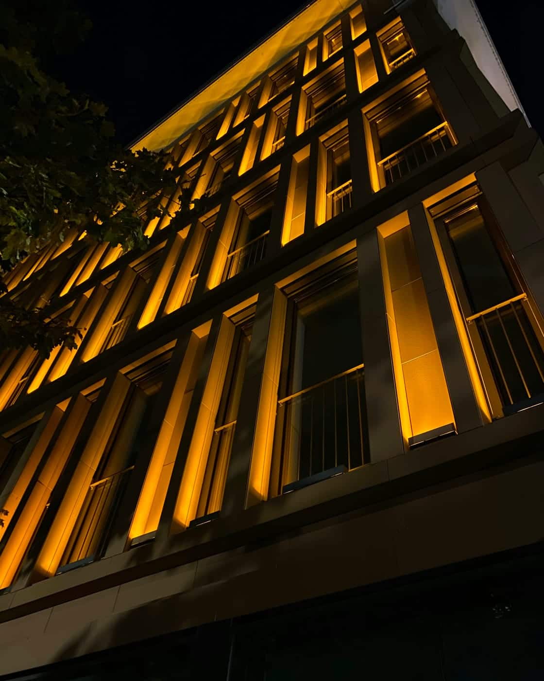 Warm linear lighting picking out the bays of a building facade after dark
