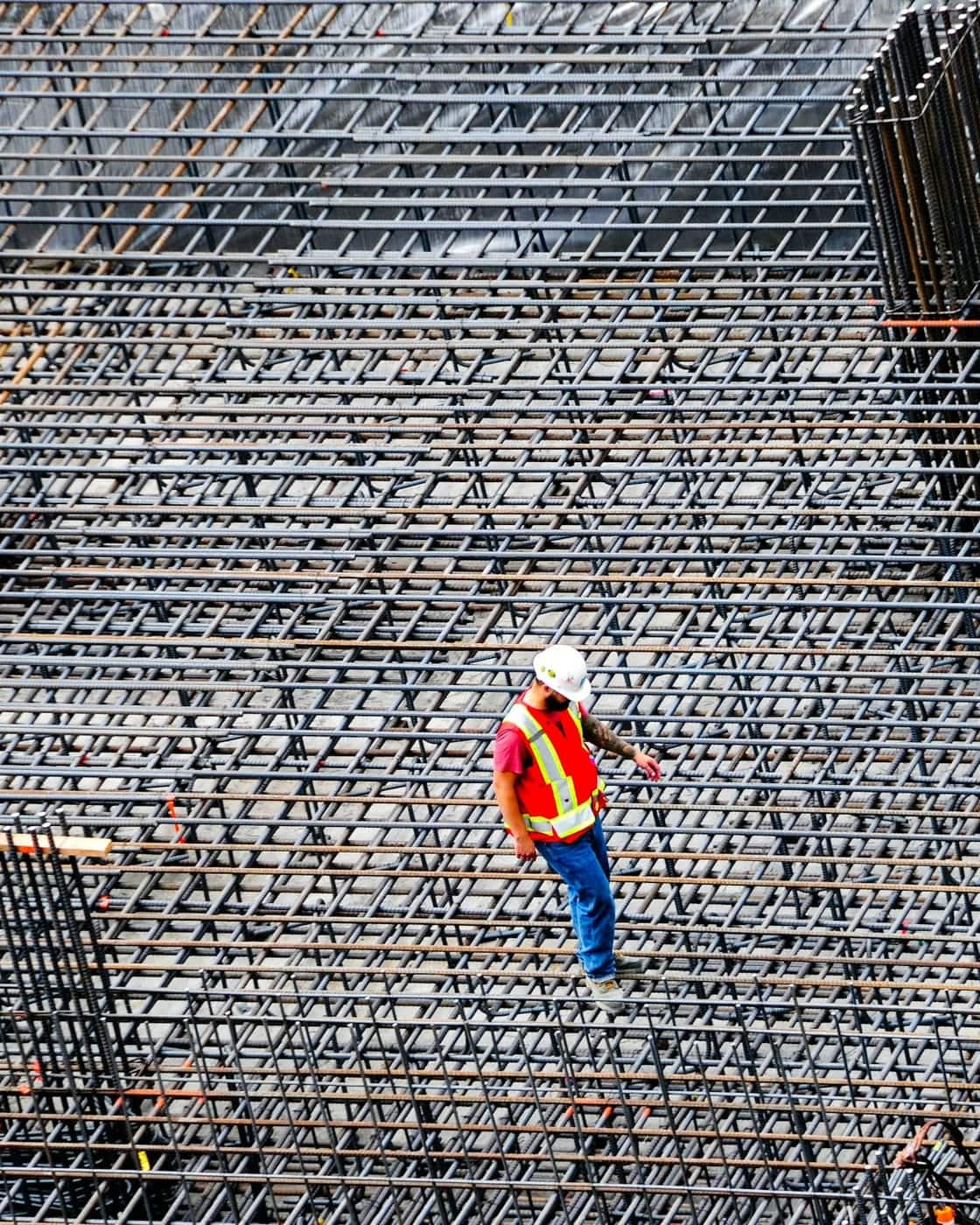 مهندس بزي عالي الوضوح يتفقّد شبكة تسليح كثيفة ممتدة على بلاطة كبيرة.
