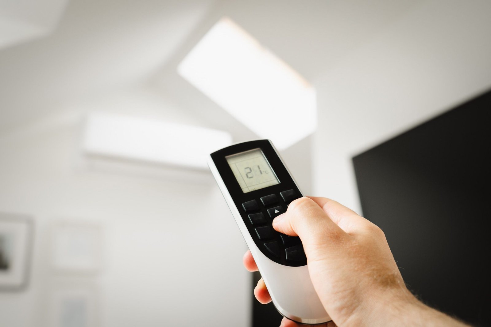 Services Close-up of a man using a remote to control air conditioning indoors.